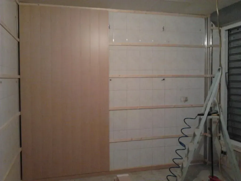Construcción de un armario empotrado, con paneles de madera y montantes a la vista. Una escalera se encuentra cerca.