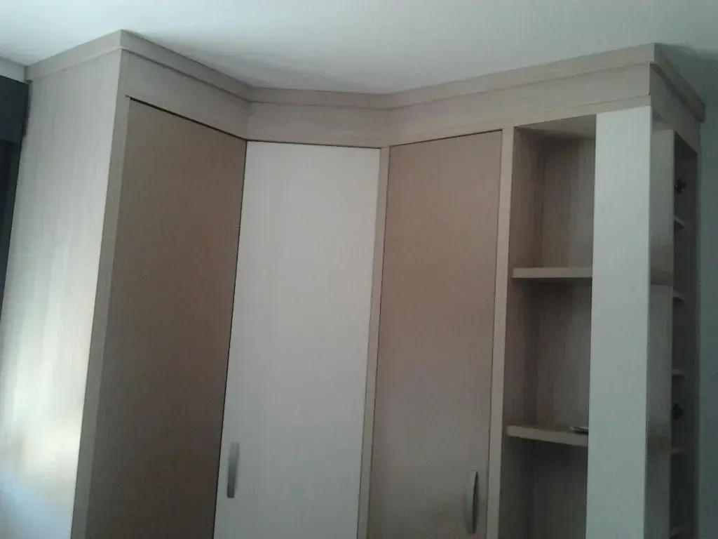 Armario empotrado con puertas y estantes en tonos crema y beige, rematado con moldura de techo.