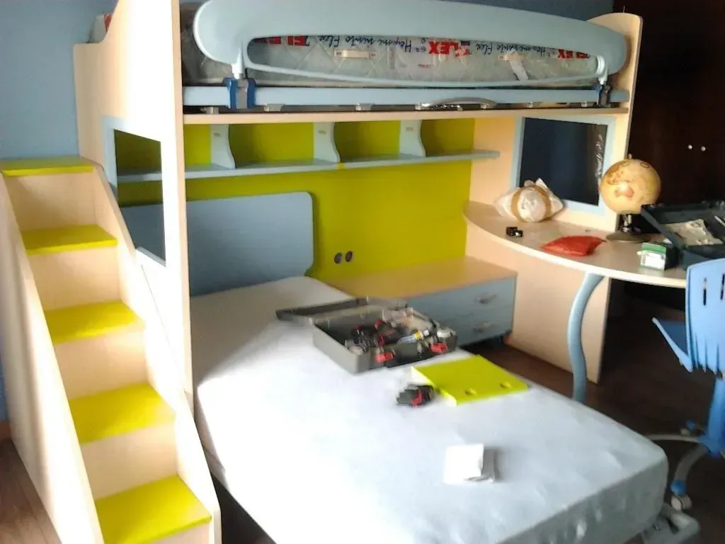 Una litera con detalles amarillos, escritorio, estanterías y escaleras en una habitación muy iluminada.