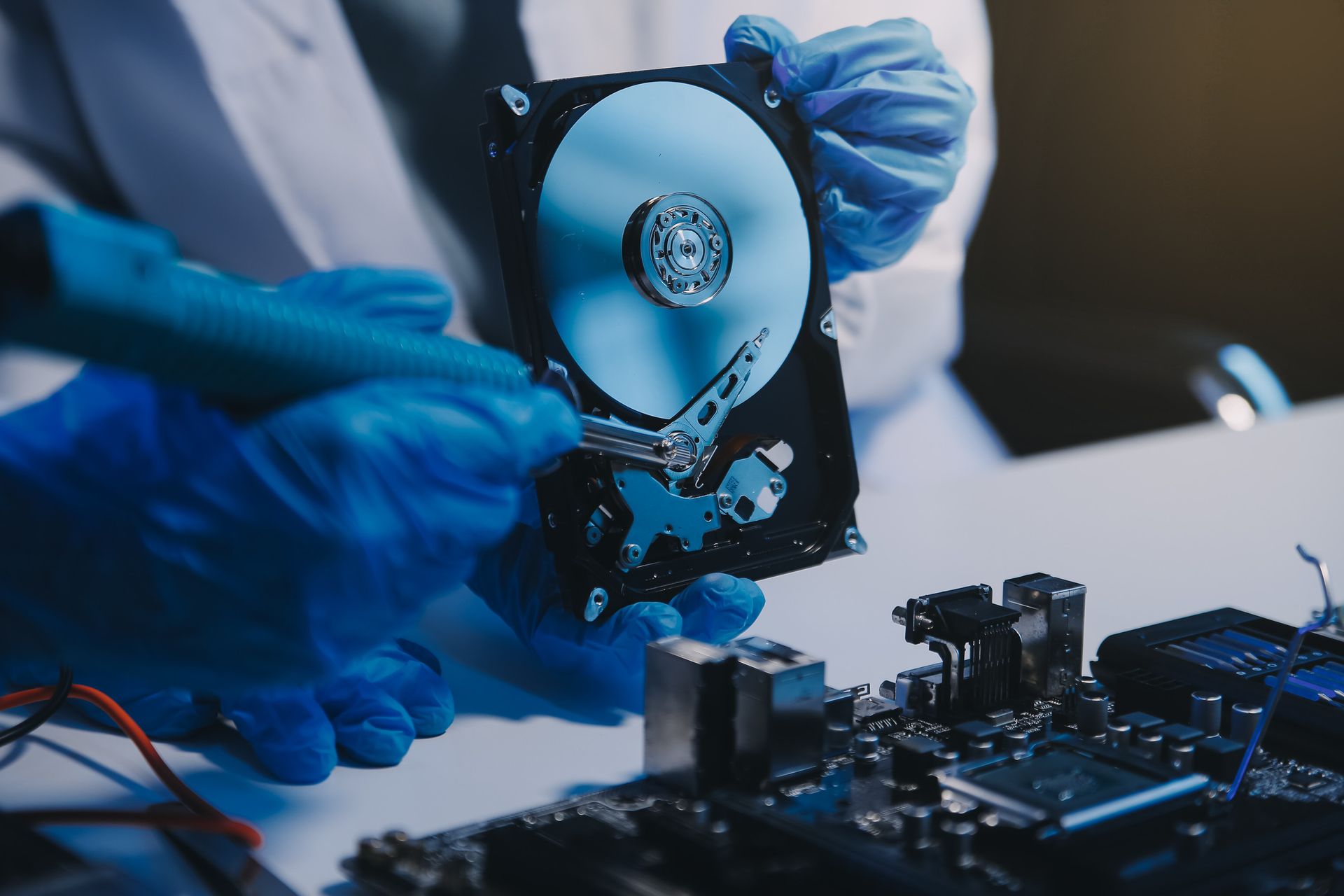 Manos con guantes azules sosteniendo y examinando un disco duro y partes de una computadora.