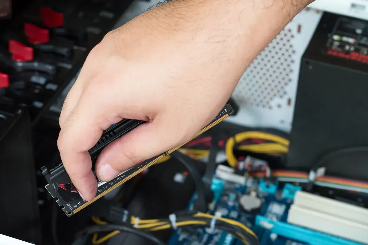 Mano instalando una memoria RAM en la placa base de una computadora, concentrándose en la RAM y la mano.