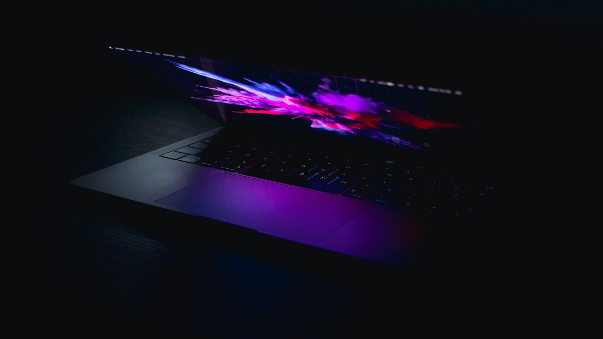Computadora portátil con pantalla de luz violeta y rosa vibrante en pantalla y teclado.
