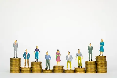 Un grupo de personas en miniatura paradas encima de pilas de monedas.