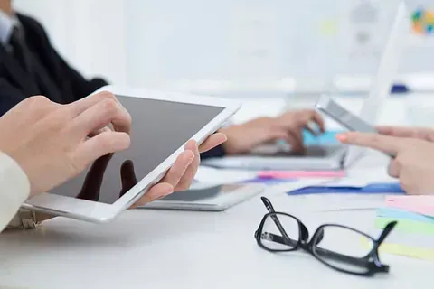 Un grupo de personas está sentada en una mesa usando una tableta y un teléfono celular.