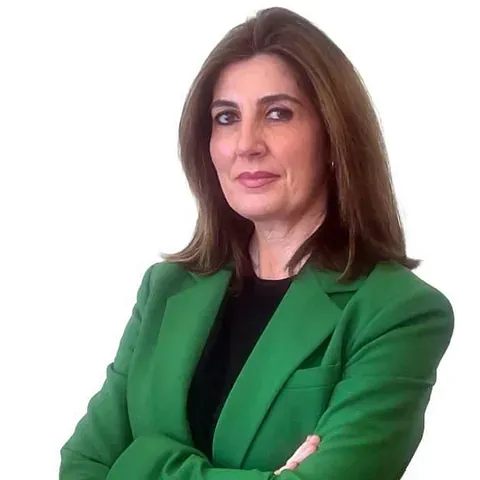 Una mujer con una chaqueta verde está de pie con los brazos cruzados.