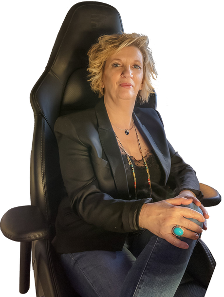 Personne assise dans un fauteuil noir à haut dossier, portant un blazer foncé et un jean, les mains jointes avec une bague turquoise.