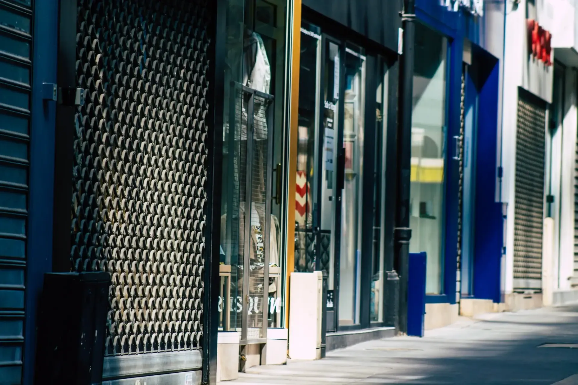 Escaparates cerrados con puertas de seguridad metálicas que reflejan la luz del sol en una calle de la ciudad.