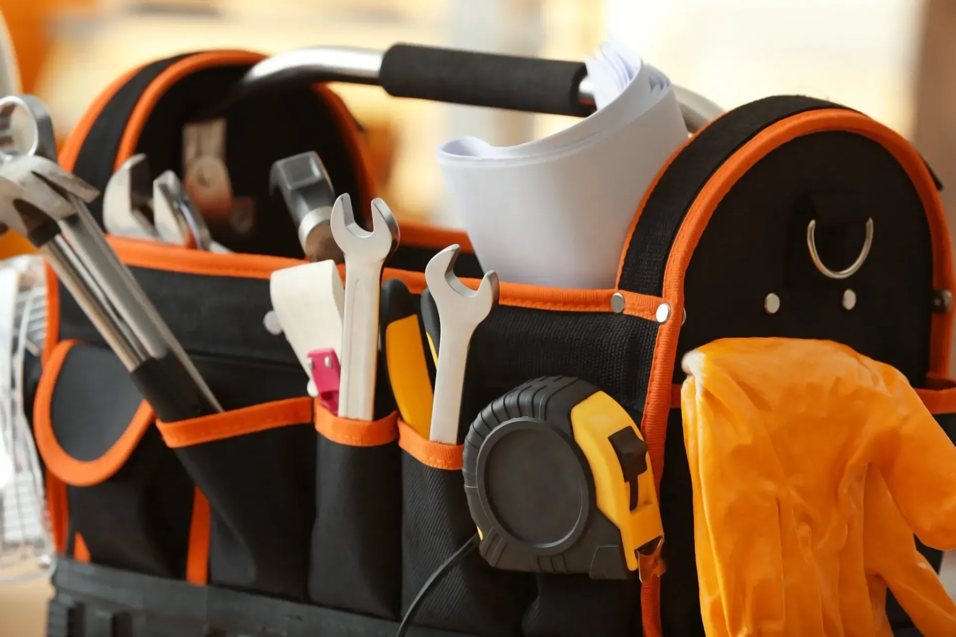 Bolsa de herramientas negra y naranja con herramientas variadas, incluidas llaves y una cinta métrica.