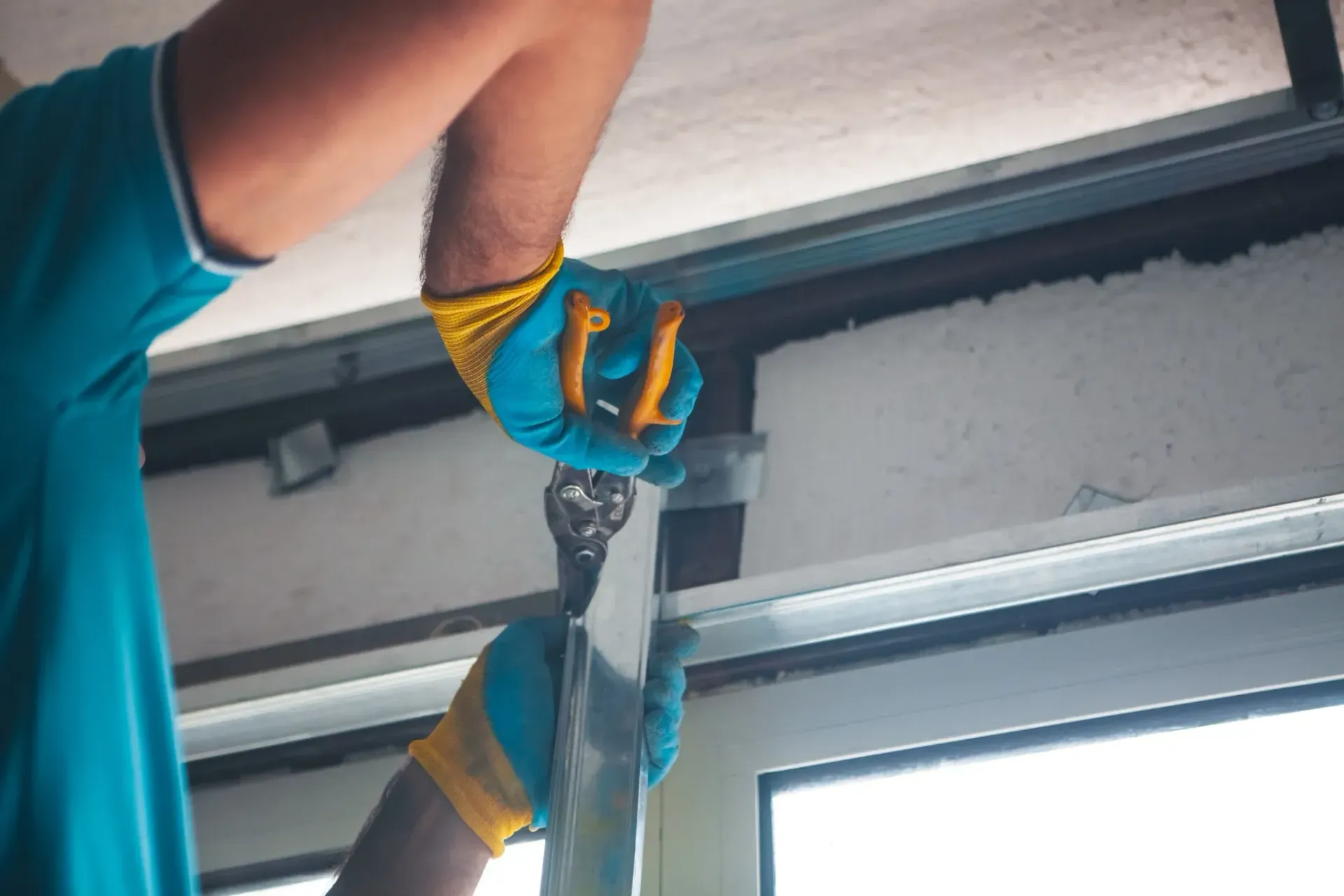 Persona con camisa azul y guantes utilizando herramientas para trabajar en una estructura metálica.