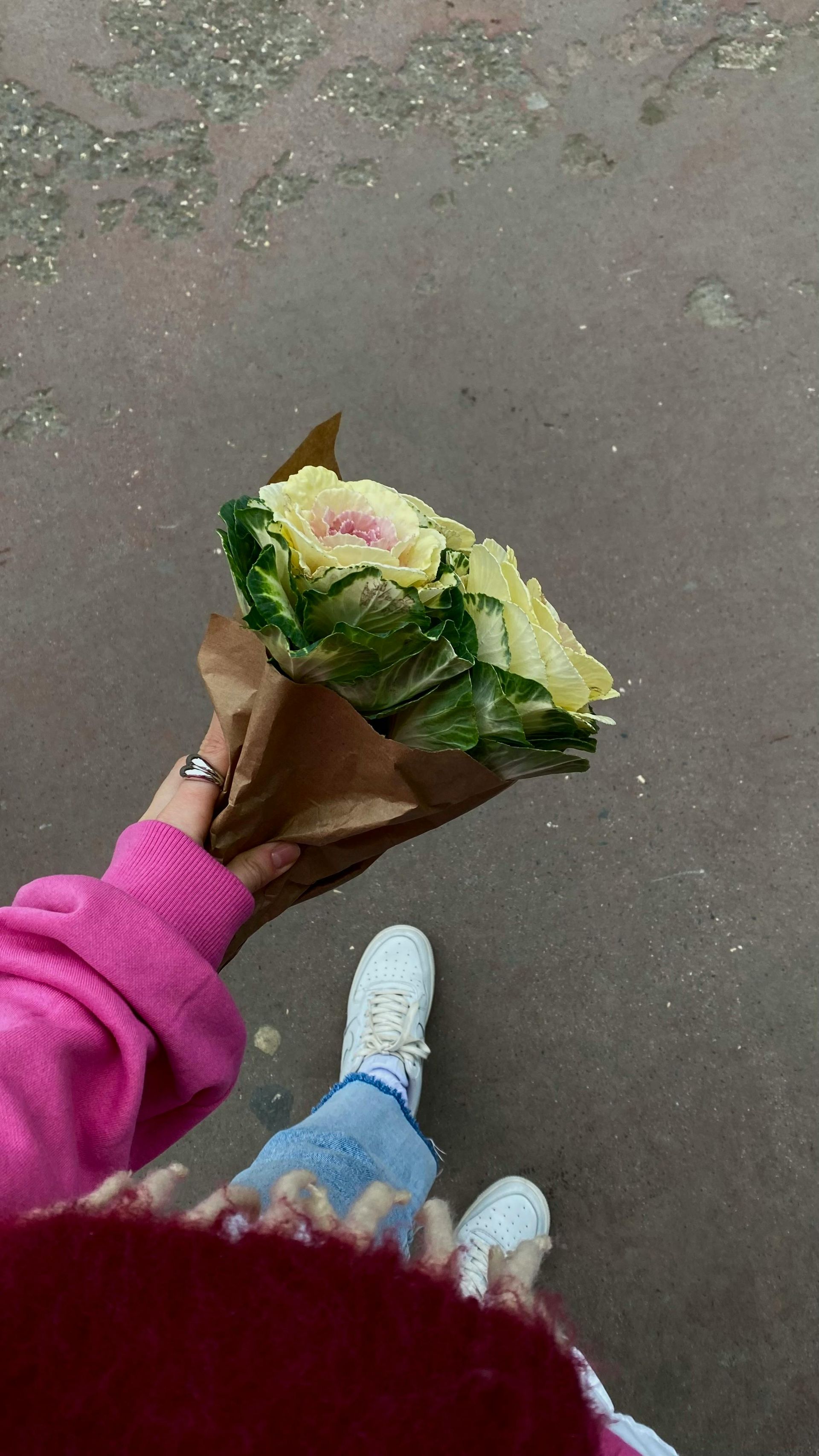 Vue plongeante sur un bouquet de fleurs jaunes aux feuilles vertes tenu par une personne debout sur un trottoir.