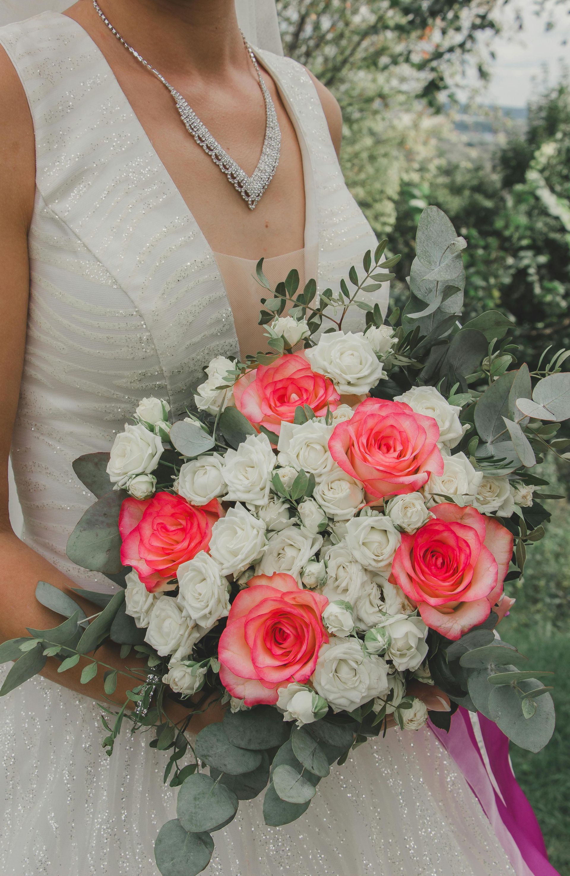 La mariée tient un bouquet de roses roses, de fleurs blanches et de feuillage d'eucalyptus sur sa robe blanche.