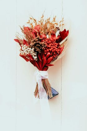 Bouquet de fleurs séchées rouges enveloppé dans du papier blanc, accroché à un mur blanc