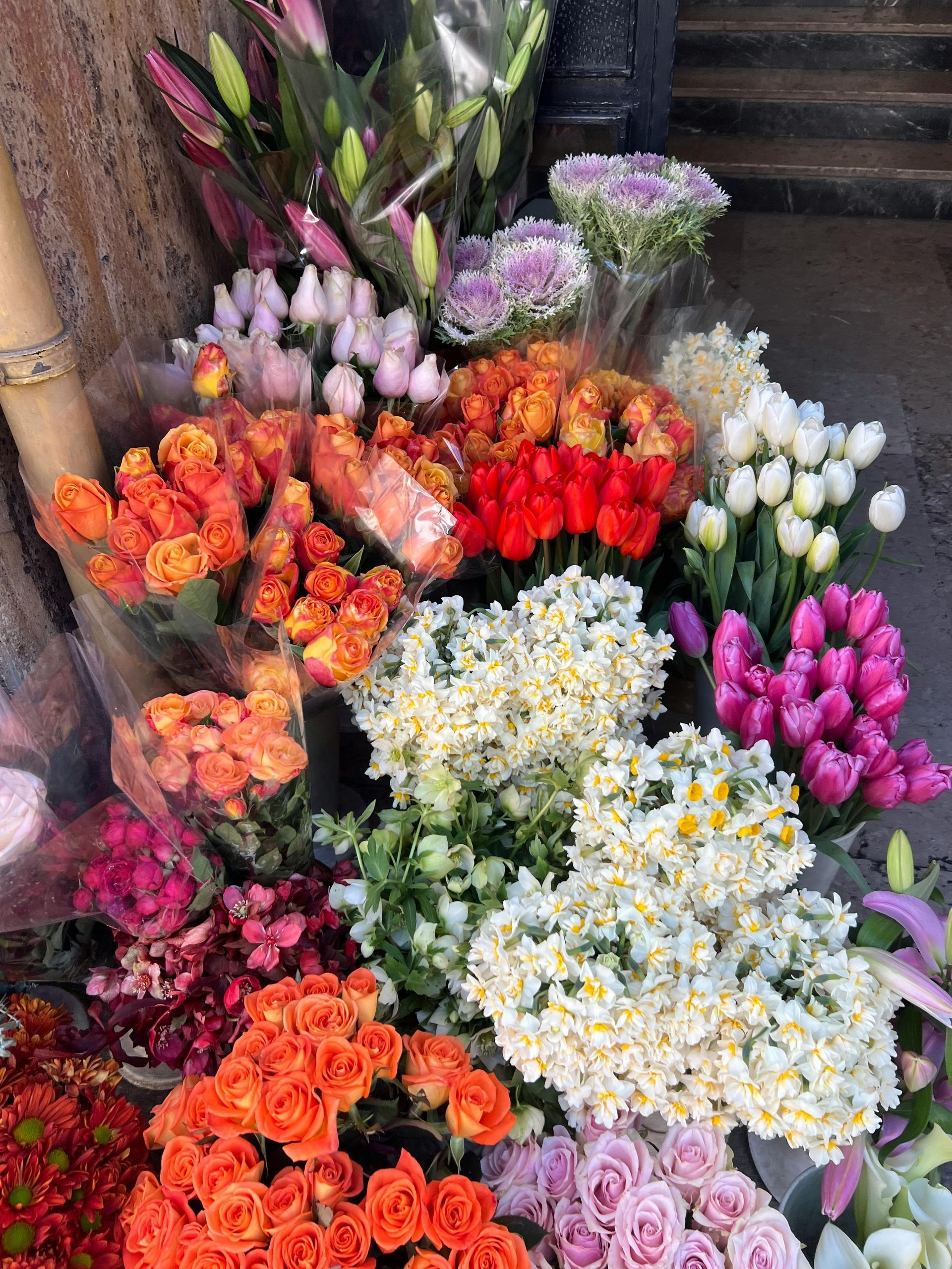 Un bouquet coloré de fleurs rouges, orange, blanches, roses et violettes, disposé sur un étal de marché.