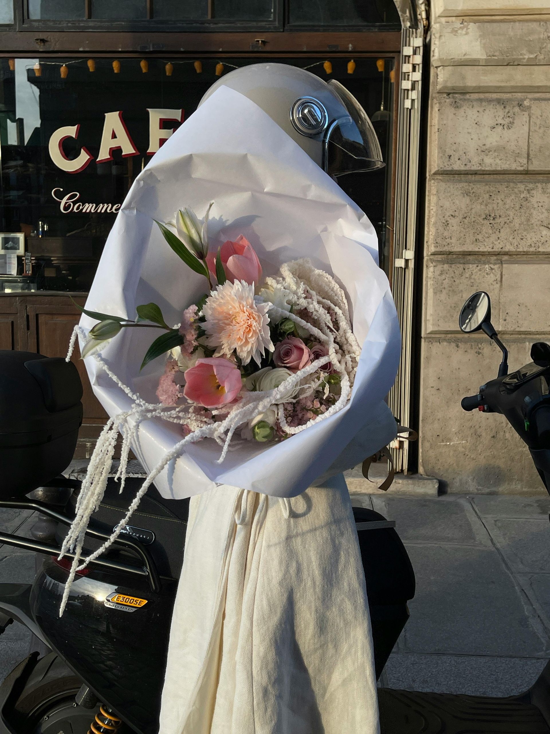 Bouquet de fleurs roses et blanches emballées dans du papier, tenu devant la vitrine d'un café.