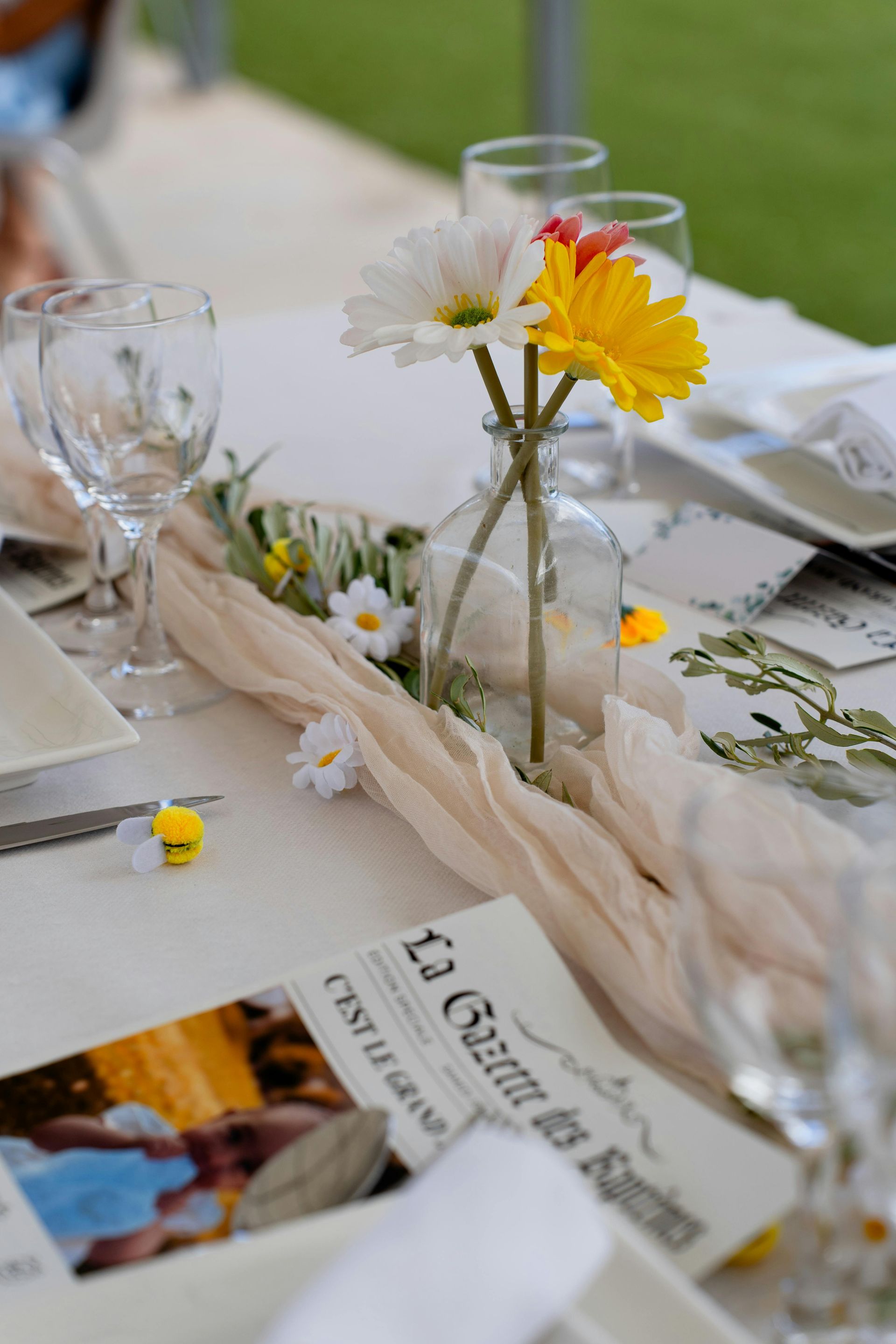 Table blanche dressée avec un vase de marguerites, des verres, des serviettes et un magazine sur la table