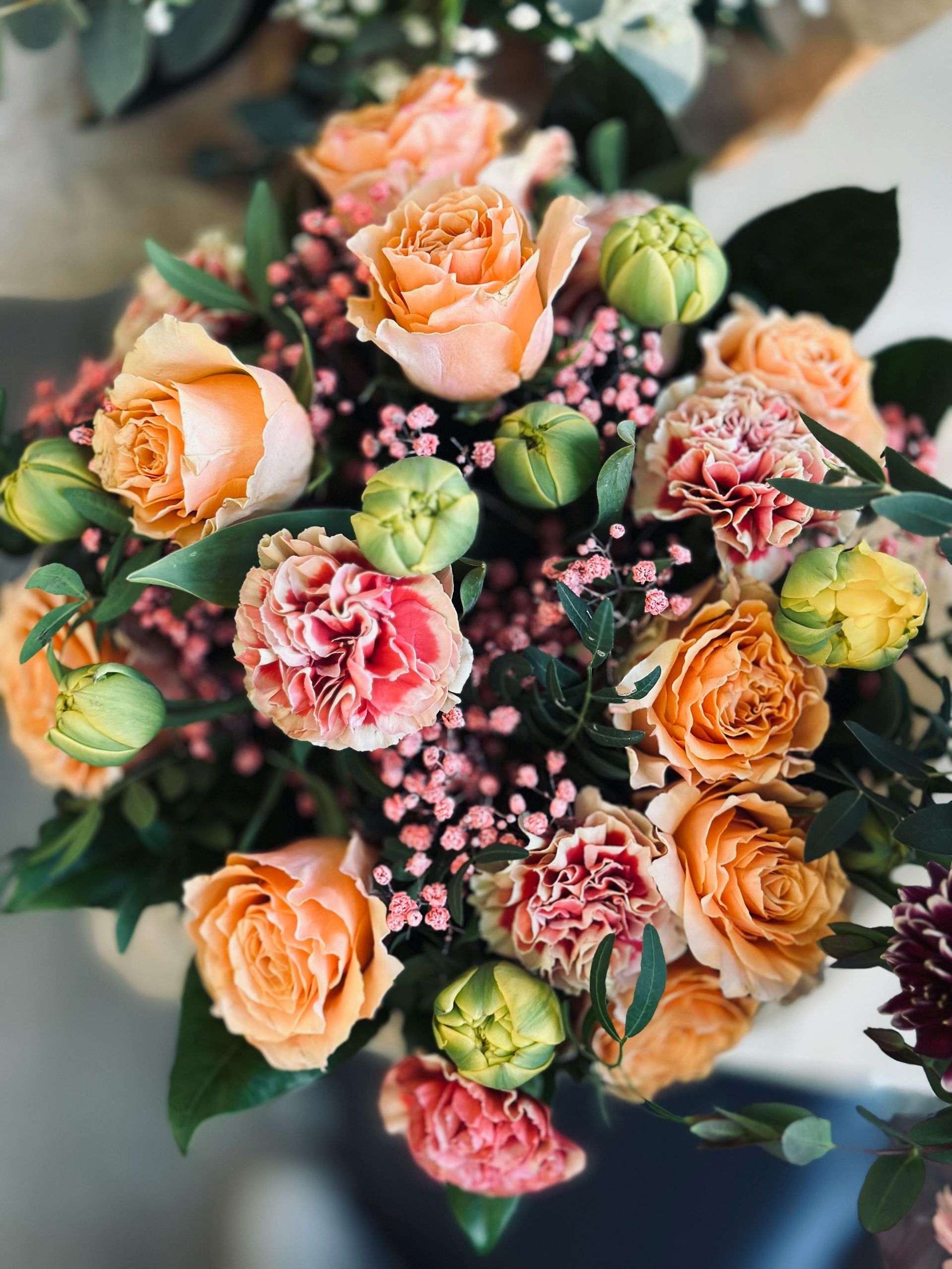 Bouquet de roses pêche, roses et corail, agrémenté de touches de vert et de gypsophile.