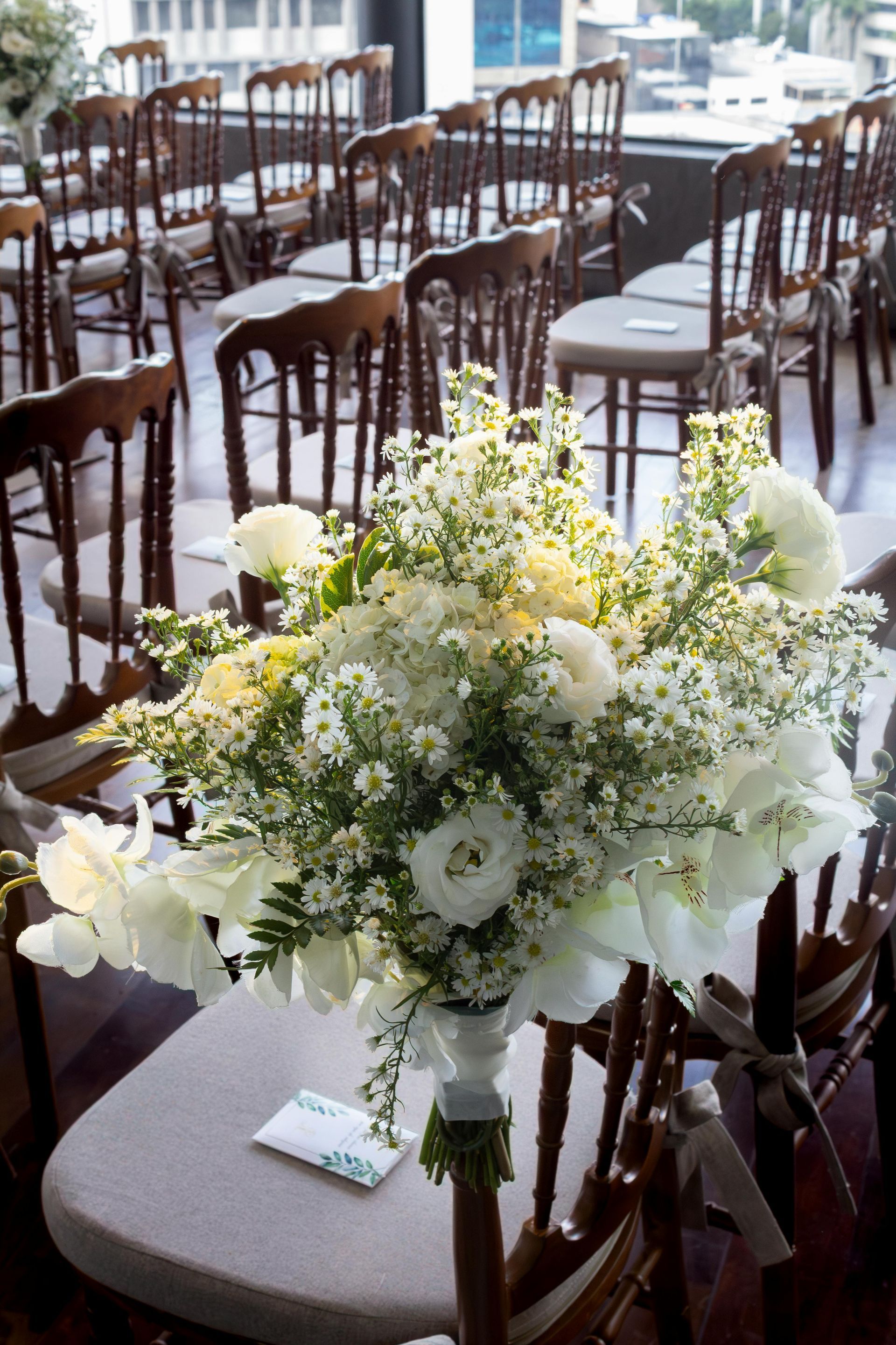 Centre de table floral dans une salle de réception lumineuse avec des rangées de chaises en bois
