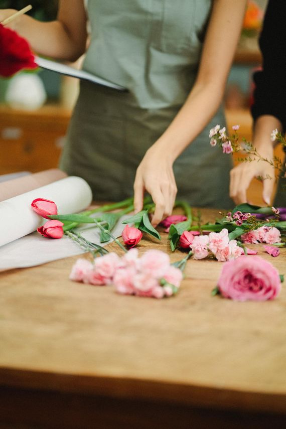 Une personne arrange des fleurs roses sur une table en bois avec du matériel de fleuriste