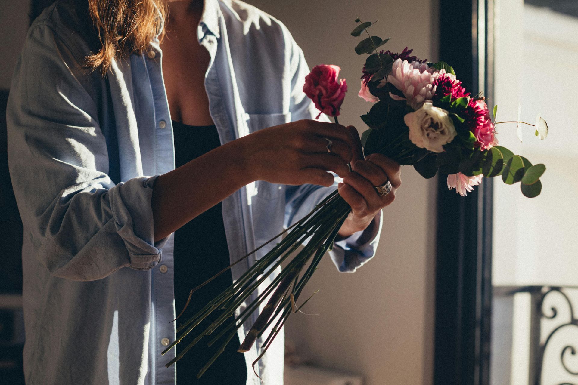 Une personne arrange un bouquet de fleurs roses et blanches près d'une fenêtre ensoleillée