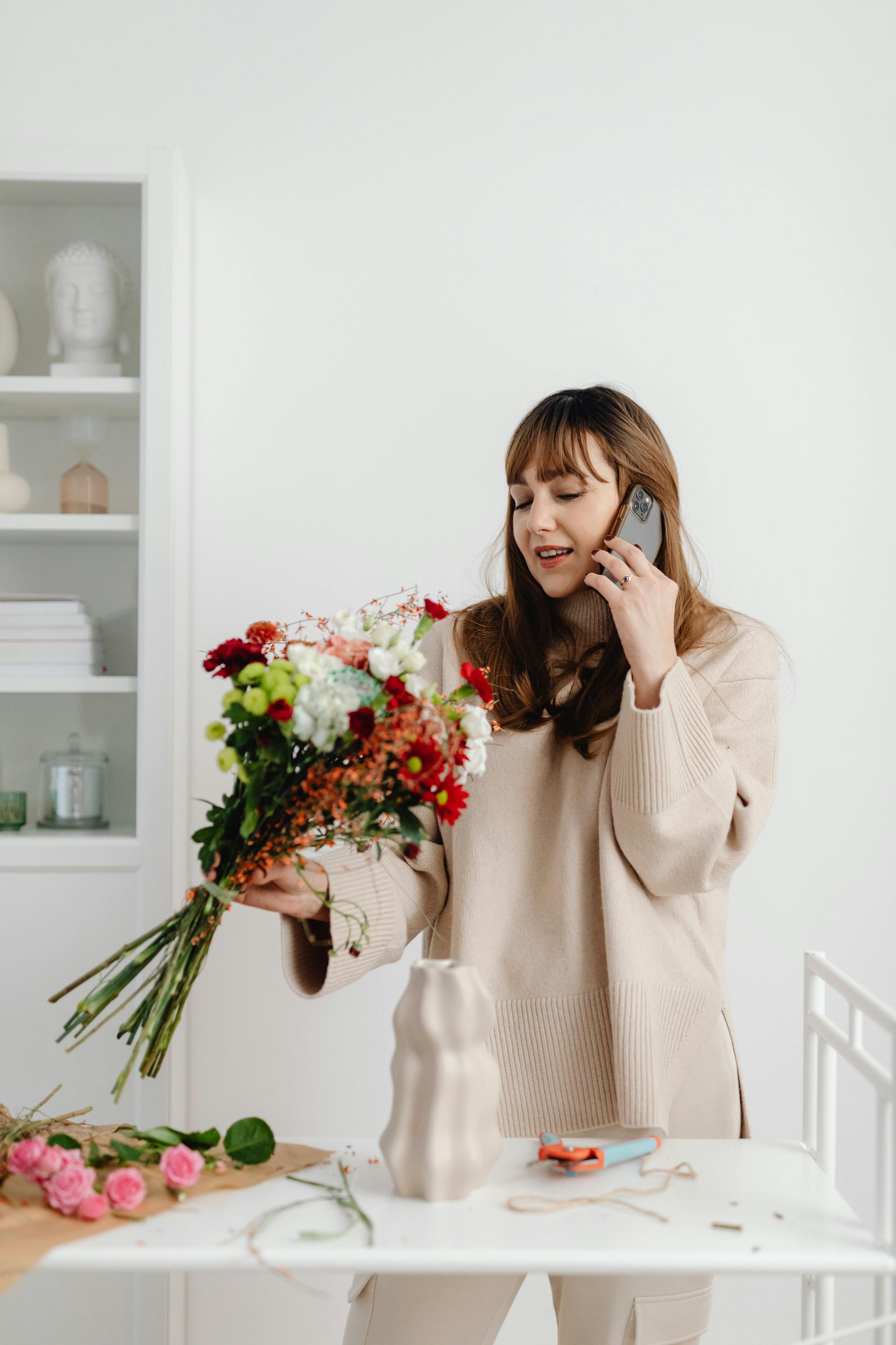 Une femme arrange un bouquet de fleurs colorées sur une table blanche dans une pièce lumineuse.