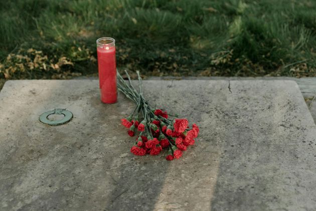 Une bougie rouge et des fleurs rouges ont été déposées sur une dalle commémorative en béton à l'extérieur.