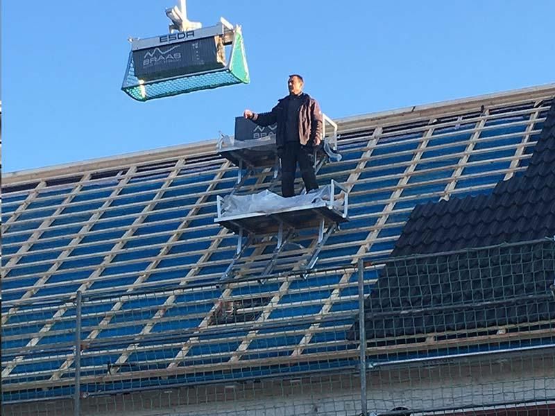 Ein Mann steht auf einem Dach und hebt mit einem Kran einen Container an.