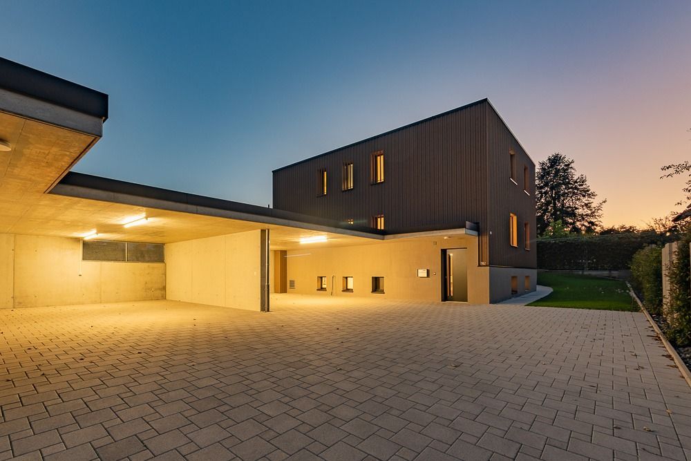 Modernes Hausäußeres in der Abenddämmerung mit warmem Verandalicht und einem gepflasterten Innenhof