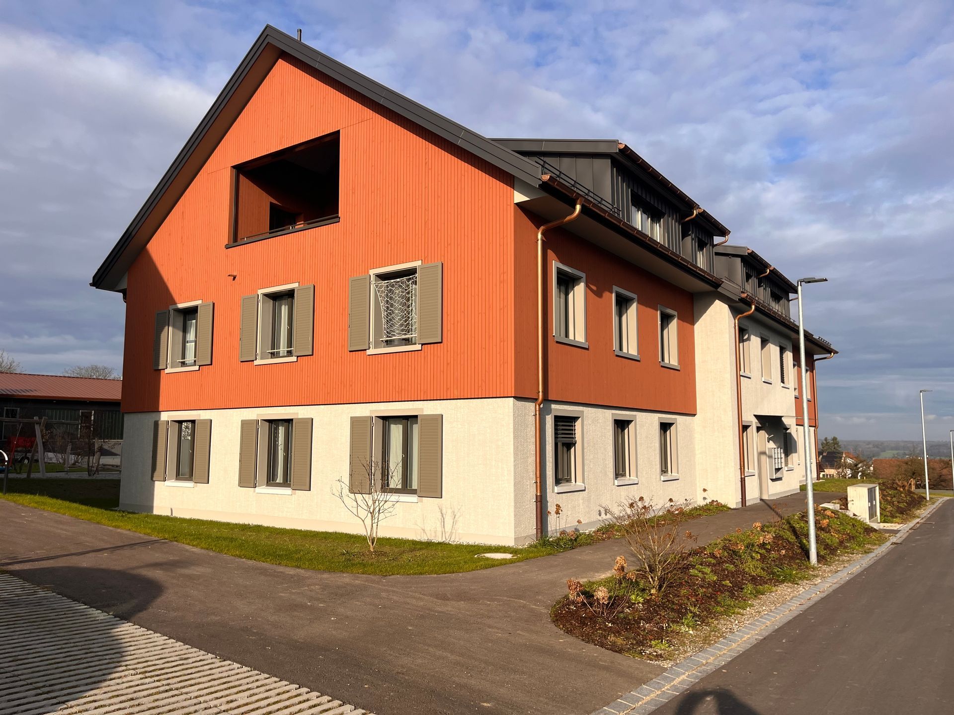 Modernes zweistöckiges orange-weißes Wohnhaus neben einer Straße an einem sonnigen Tag