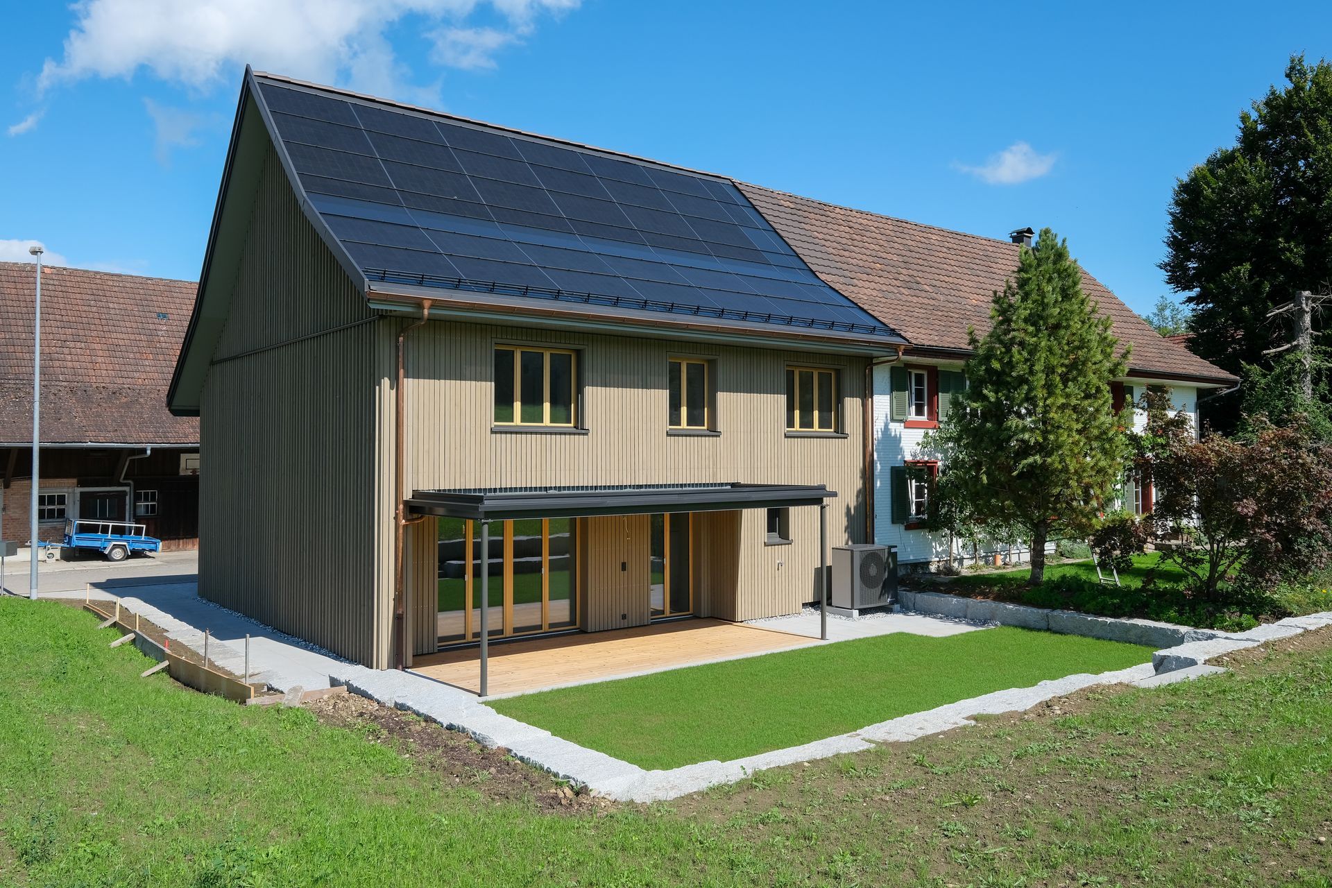 Modernes Haus mit Solarpaneelen, Holzverkleidung und kleinem Rasen an einem sonnigen Tag