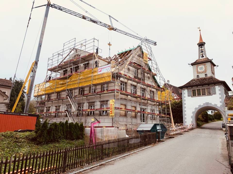 Historisches Gebäude im Umbau, Kräne neben einem weissen Uhrturmtor an einer schmalen Strasse