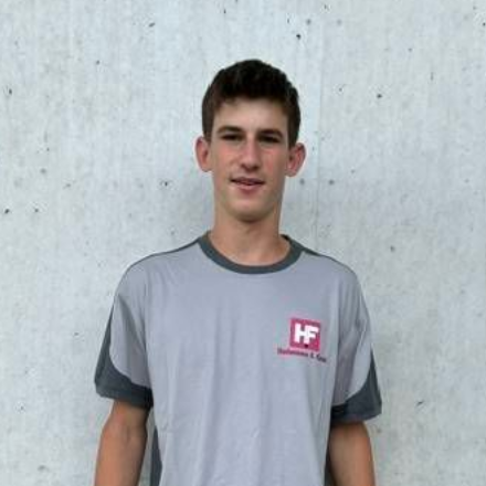 Ein Mann, der an einer Betonwand steht, trägt ein graues T-Shirt und graue Cargoshorts.
