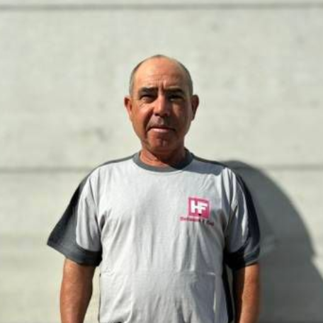 Ein Mann steht an einer hellgrauen Wand, er trägt ein graues T-Shirt und Shorts und hat die Hände an den Seiten.