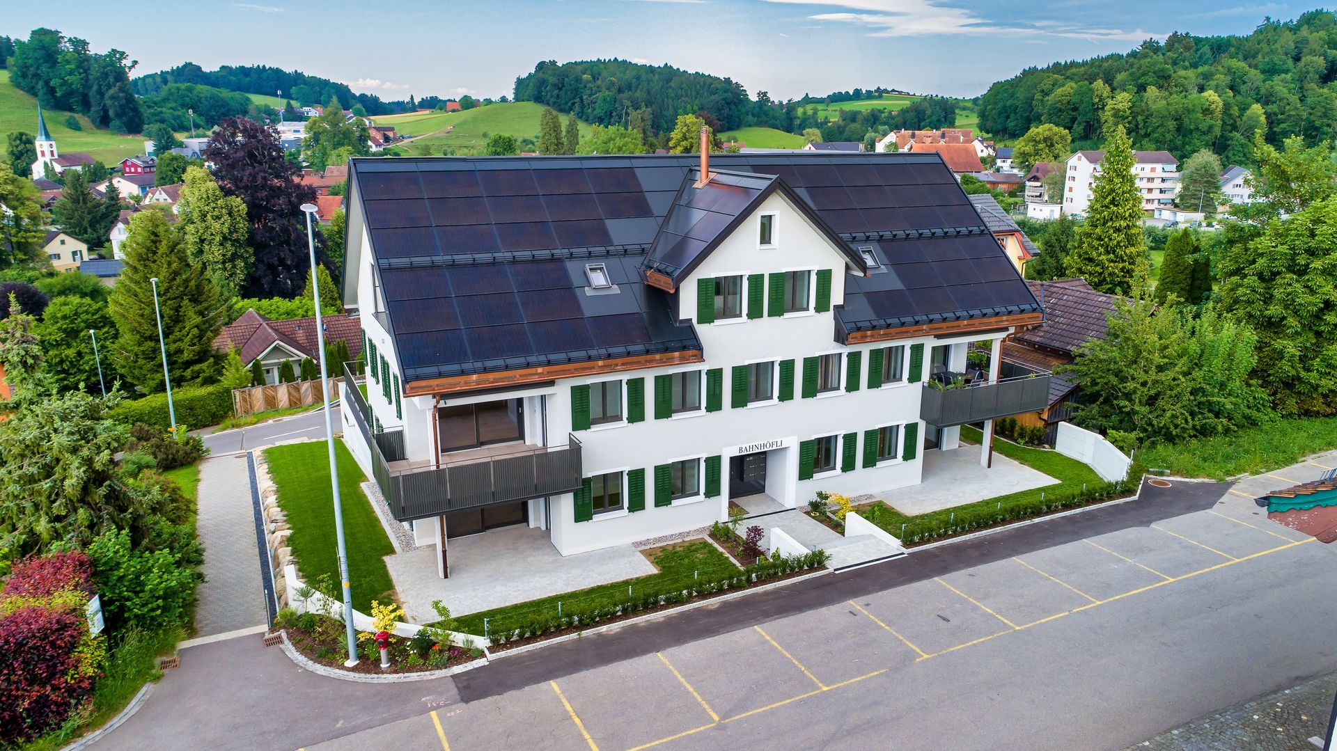 Luftaufnahme eines weißen Hauses mit Solarpaneelen neben einer Straße und grüner Landschaft.