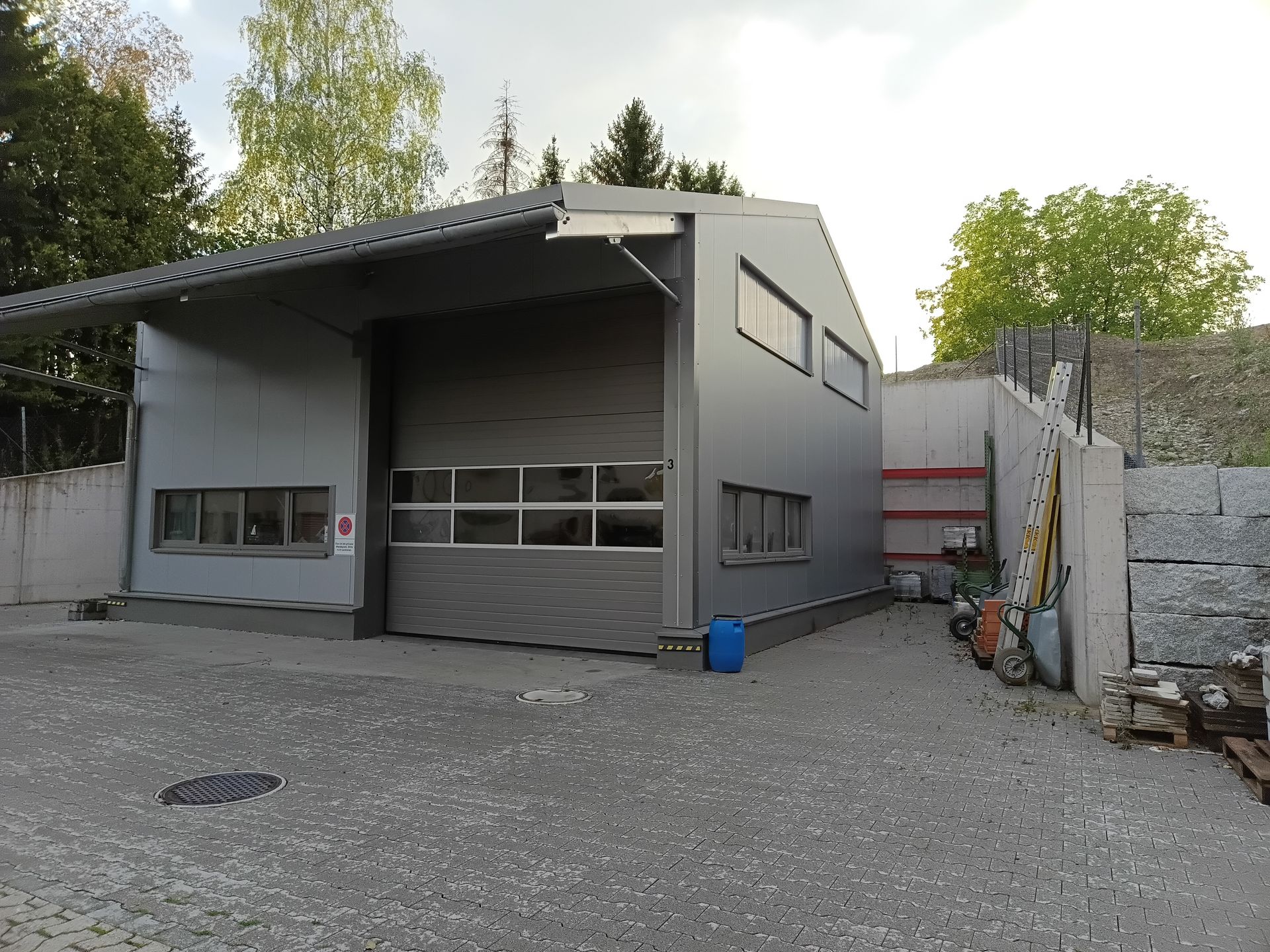 Graue Industriegarage mit großer offener Halle, kleinen Fenstern und Kieshof im Außenbereich