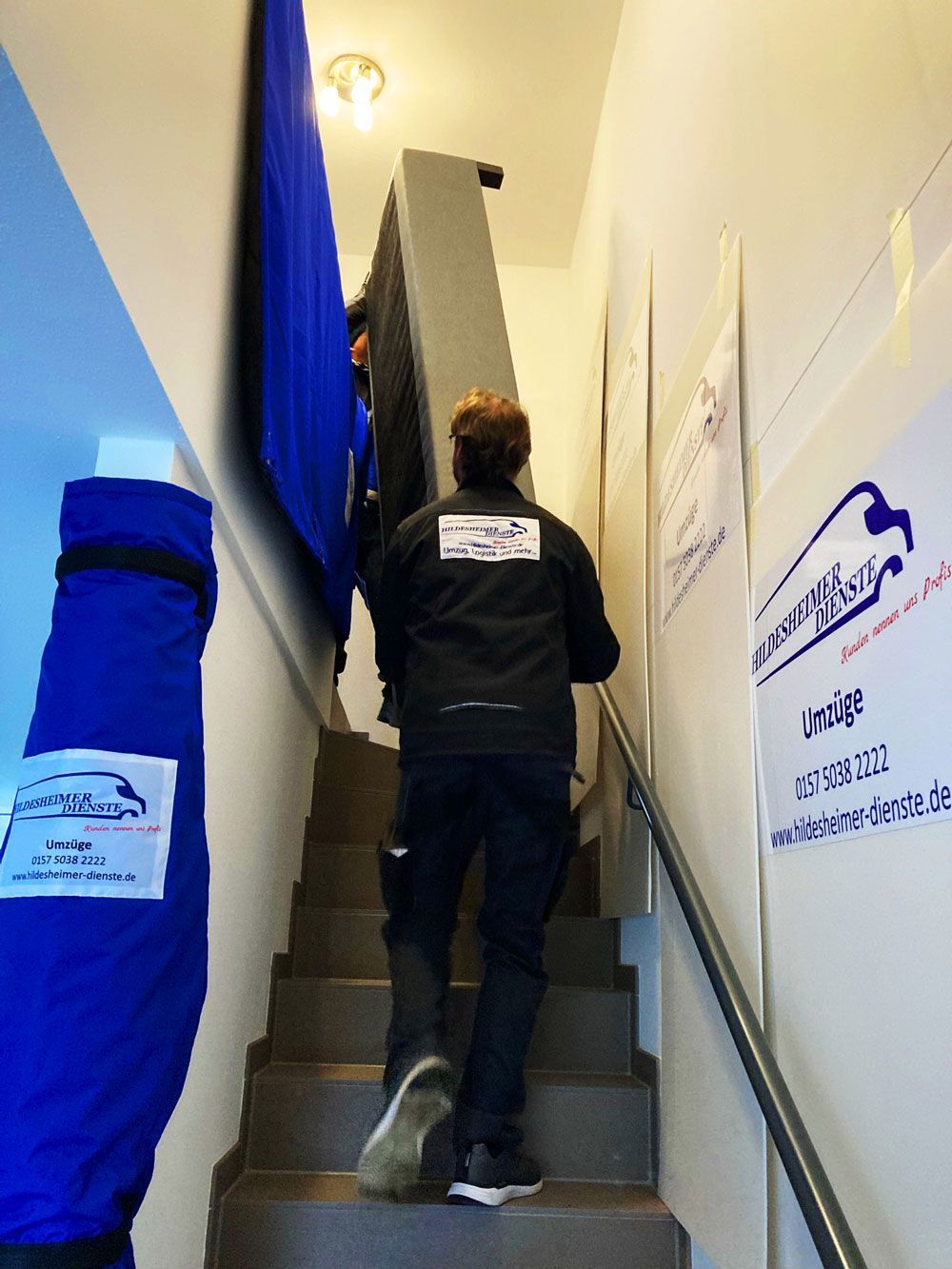 Zwei Mitarbeiter von unserem Umzugsunternehmen in Hildesheim tragen Möbel auf einer Treppe.