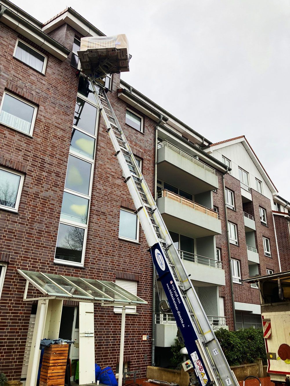 Ein Möbellift im Einsatz an einem modernen Wohngebäude. Über eine lange Schiene werden Möbel oder Baumaterialien sicher in die oberen Etagen transportiert. Jetzt Umzugslift mieten in Hildesheim für einen schnellen und bequemen Umzug ohne Treppensteigen!