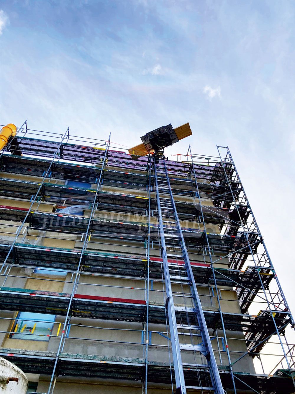 Ein Möbellift ist im Einsatz an einem eingerüsteten Gebäude. Der Möbellift transportiert Möbel oder Baumaterialien über eine lange Schiene nach oben. Ideal für den Umzug oder Renovierungsarbeiten. Jetzt Möbellift mieten in Hildesheim für einfache und sichere Transporte in höhere Etagen!