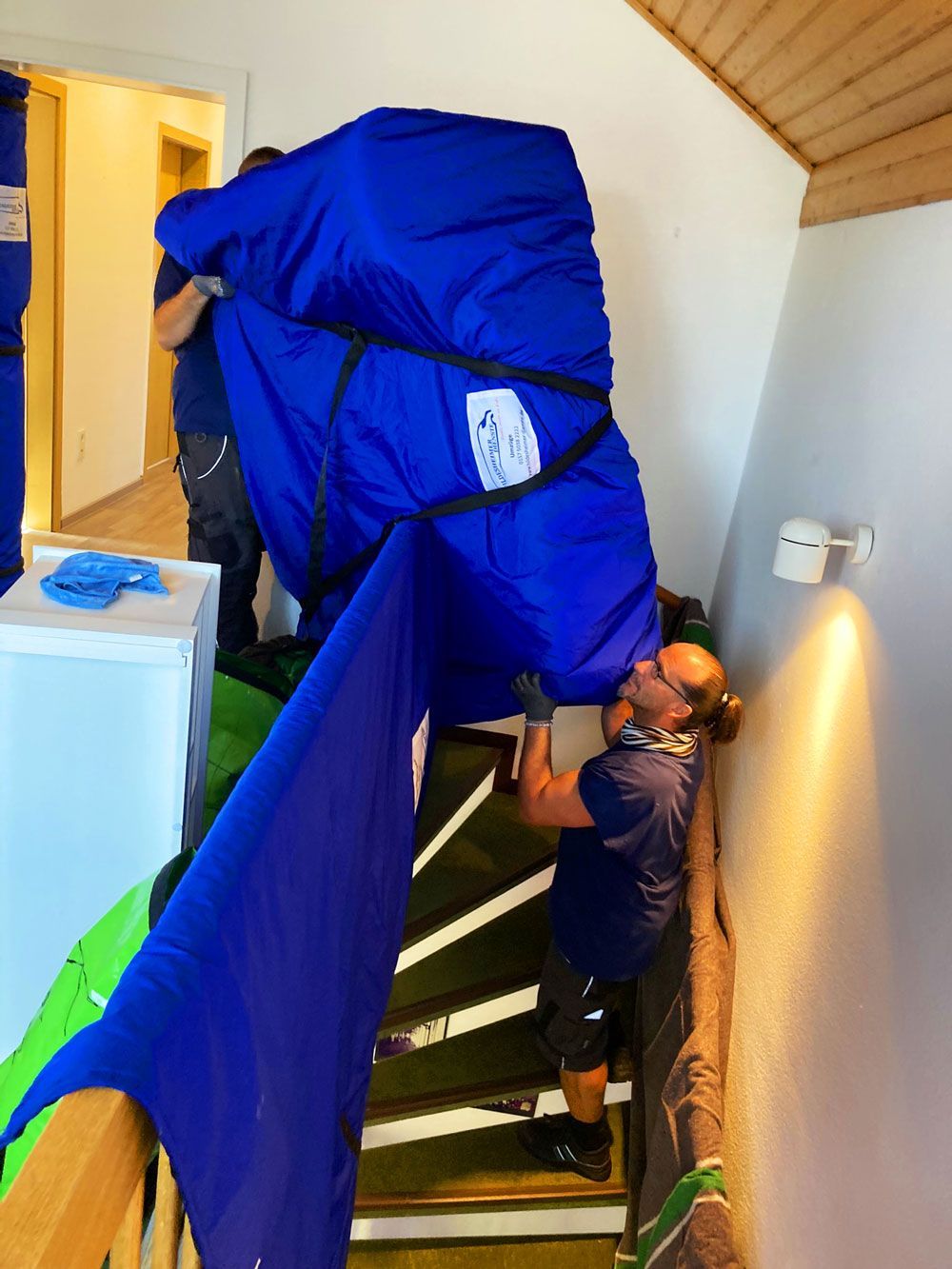 Zwei Männer von unserem Umzugsunternehmen in Hildesheim tragen gesichertes Umzugsgut auf einer Treppe. 