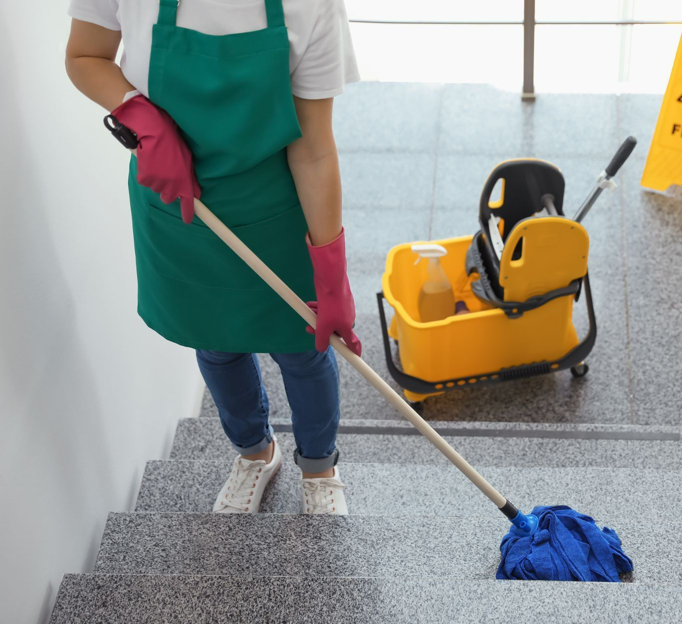 Femme avec tablier vert nettoyant une cage d'escaliers