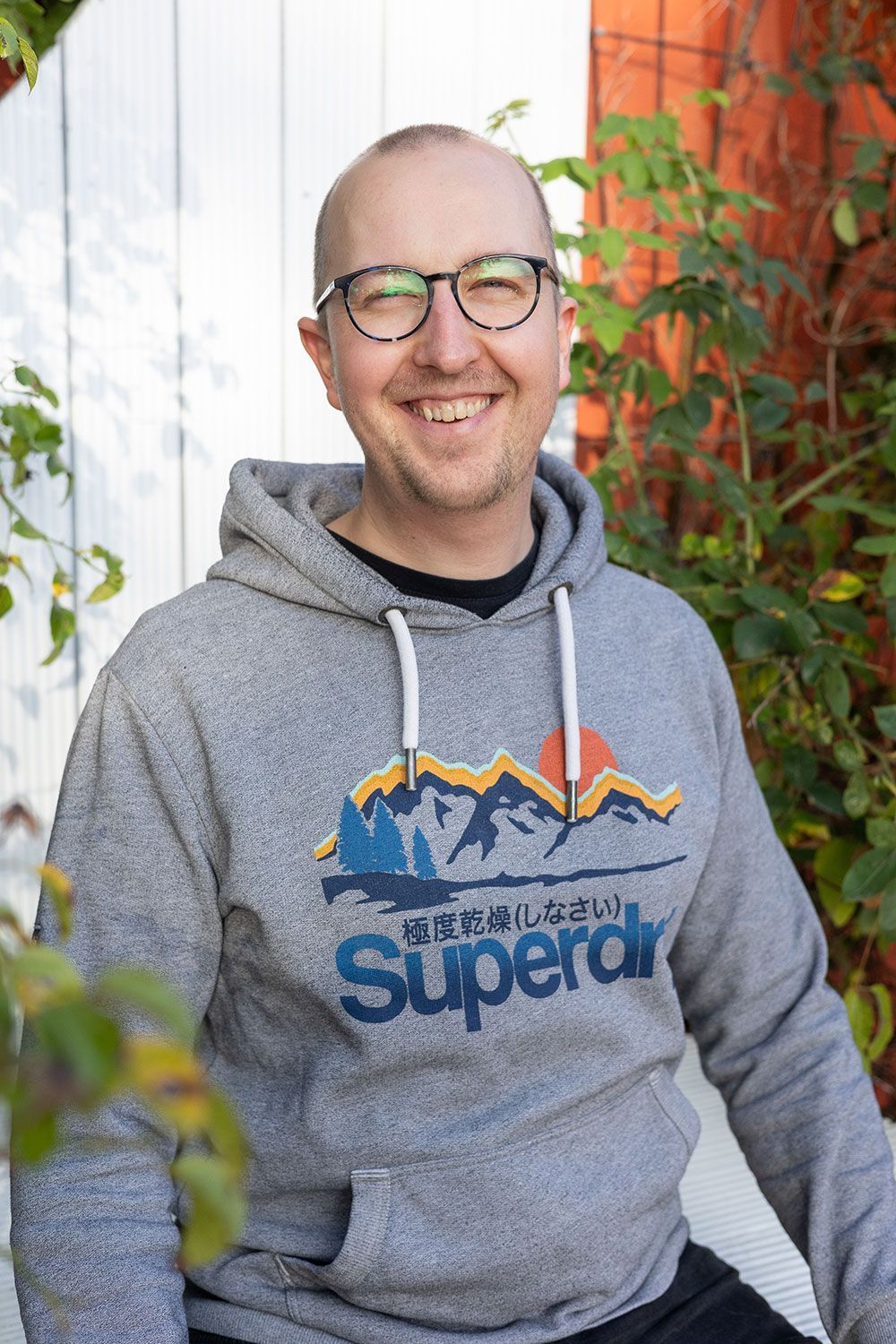 Mann mit Brille und Superdry-Kapuzenpulli lächelt im Freien.