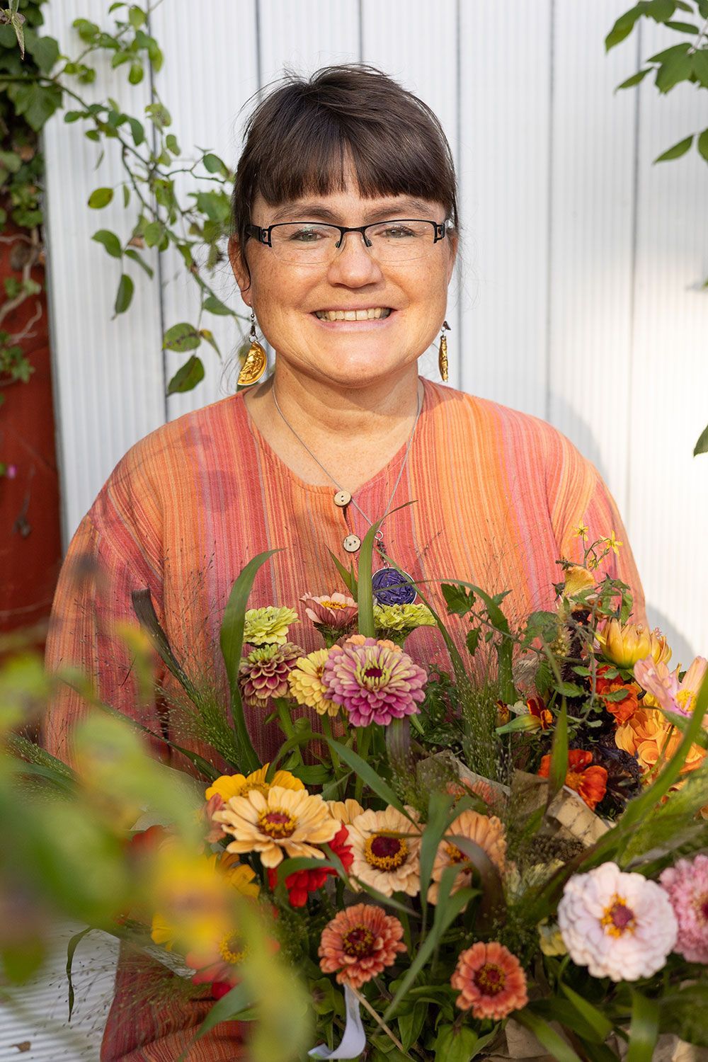 Eine Frau hält einen Strauß bunter Blumen in der Hand und lächelt, während sie in einem Garten steht.