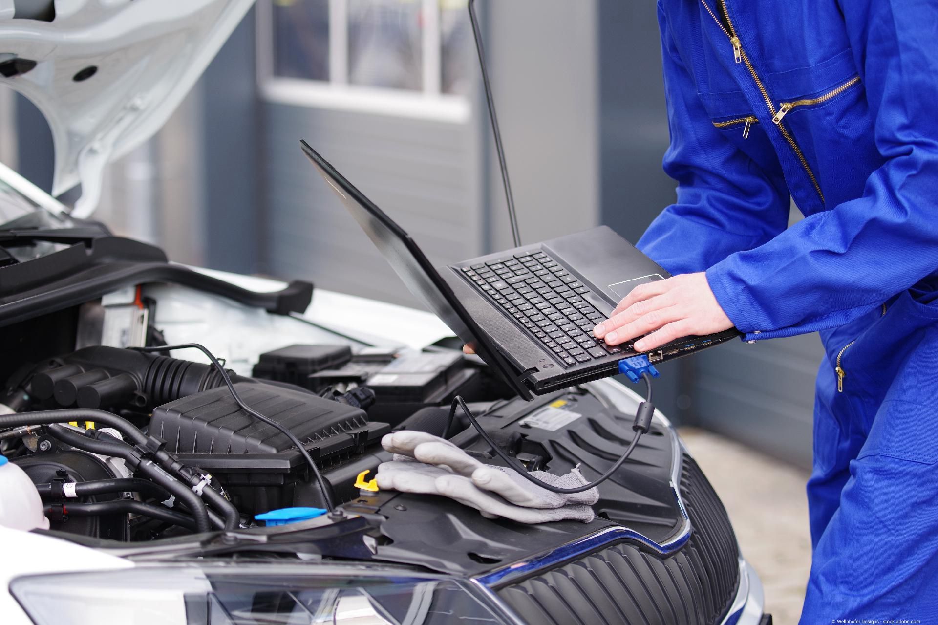 ein Mann mit einem Laptop steht vor der Motorhaube eines Autos
