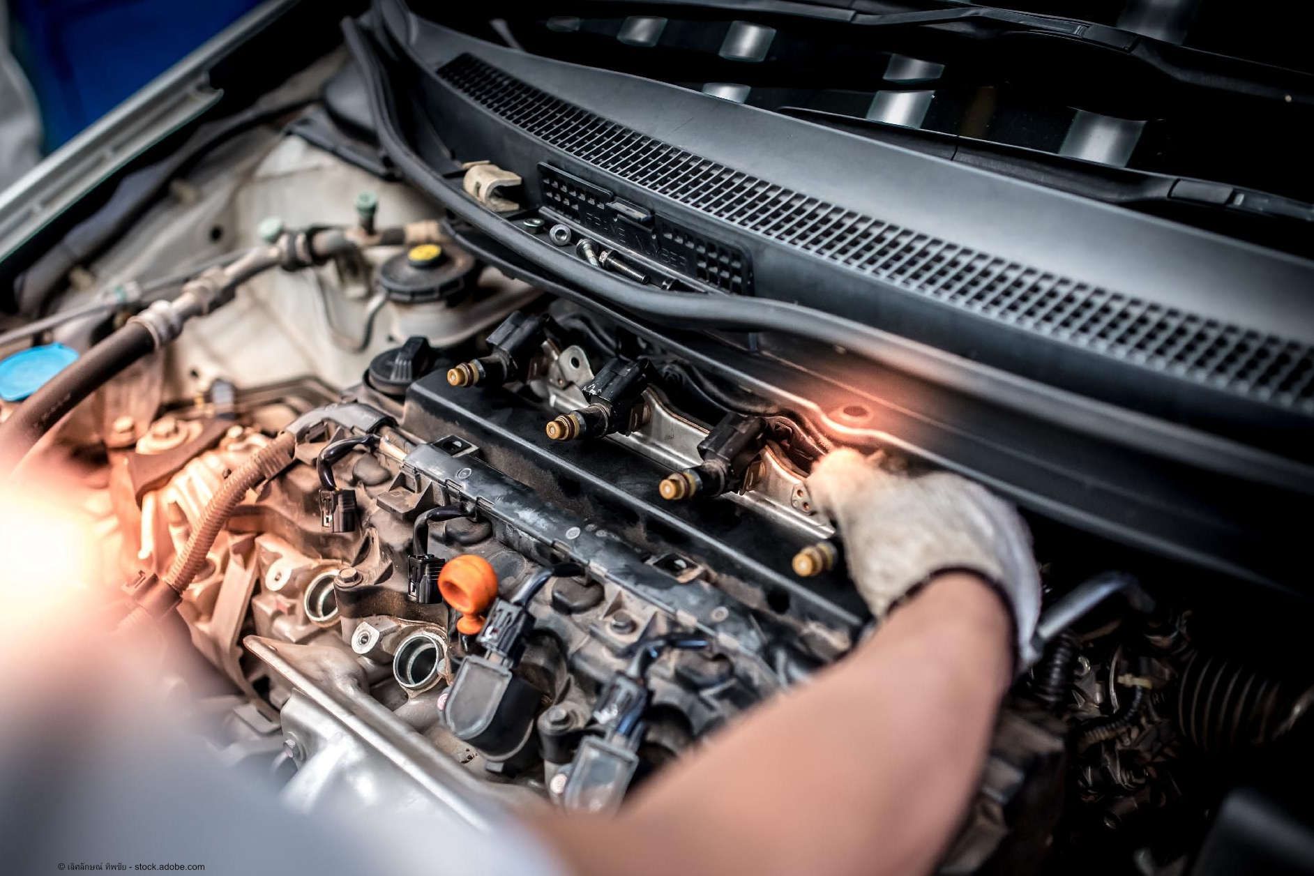 Kfz Mechaniker schaut mit einer Lampe in den Motorraum