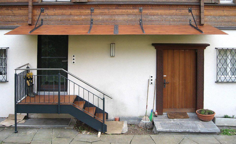 Ein weisses Gebäude mit Holztür, Treppe und Metallmarkise.