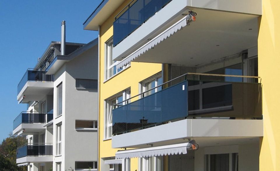 Moderne Wohngebäude mit sonnendurchfluteten Balkonen, die über Glasgeländer und Markisen verfügen.