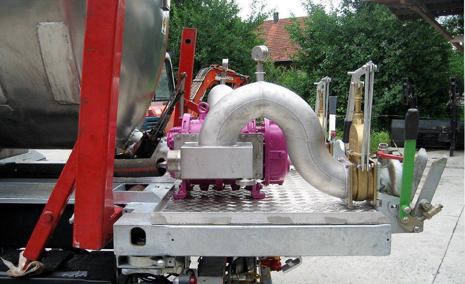 Rückansicht eines silbernen Tankwagens mit rosafarbener Pumpe und gebogenem Auspuffrohr aus Metall.