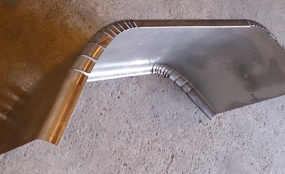 Gebogenes Metallblech mit gefalteten Kanten und Eckabschnitten, wahrscheinlich Teil eines Fahrzeugs.