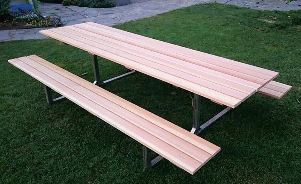 Picknicktisch mit Holzplatte und Sitzbank auf einer grünen Rasenfläche.