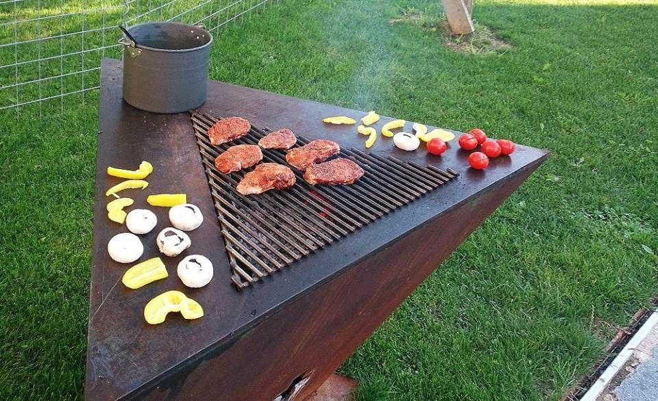 Dreieckiger Aussengrill mit Fleisch und Gemüse auf dem Rost, Topf und anderen Speisen auf dem Tisch.