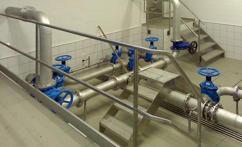 Rohre mit blauen Ventilen in einem Hauswirtschaftsraum, Metalltreppe und Geländer.
